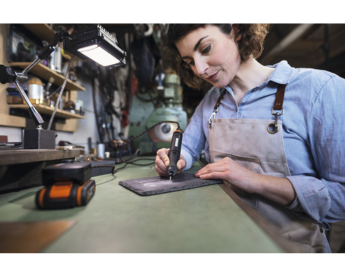 Vrouw graveert een leisteen plaat met een graveermachine op een werkbank.