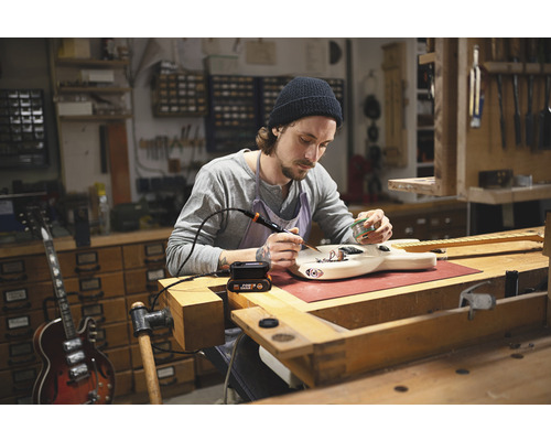 Man soldeert gitaar in werkplaats met soldeerbout
