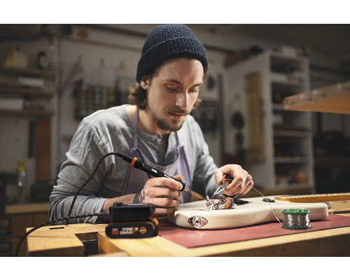 Man soldeert gitaar met een soldeerbout op een werkbank.
