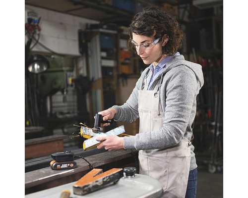 Vrouw werkt met een accukantenfrees in een werkplaats, met veiligheidsbril.