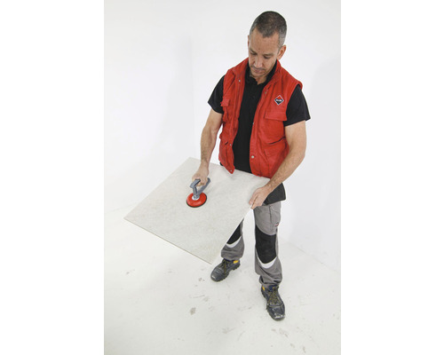 Een man tilt een tegel op met een zuignapgereedschap.