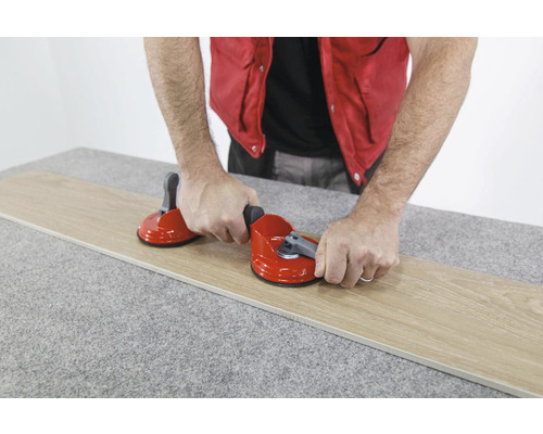 Een persoon gebruikt een dubbele zuignap om een tegel op te tillen.