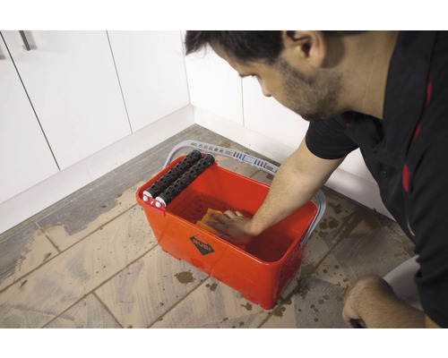 Een man maakt een tegel spons schoon in een tegel emmer.