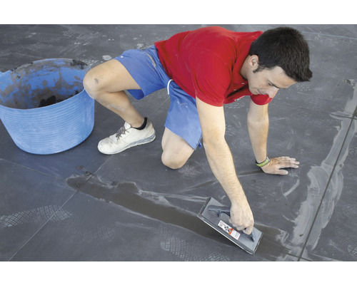 Ambachtsman voegt tegels met een voegbord in een interieur.