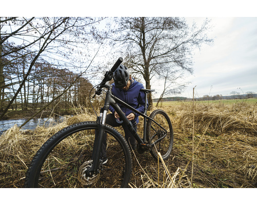 Man met helm repareert een mountainbike in de natuur.