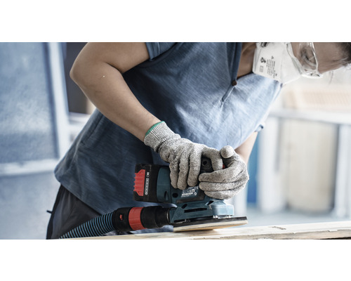 Iemand schuurt hout met een accutrilling schuurmachine, waarbij beschermende handschoenen en een stofmasker worden gedragen.