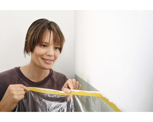 Vrouw bevestigt afdekfolie met plakband aan de muur om te schilderen