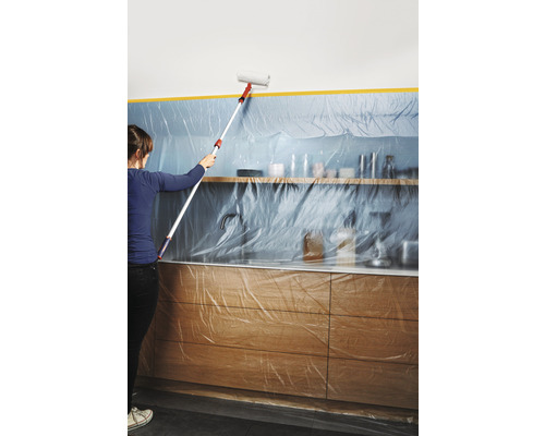 Vrouw schildert muur met verfroller in een met folie afgedekte keuken.