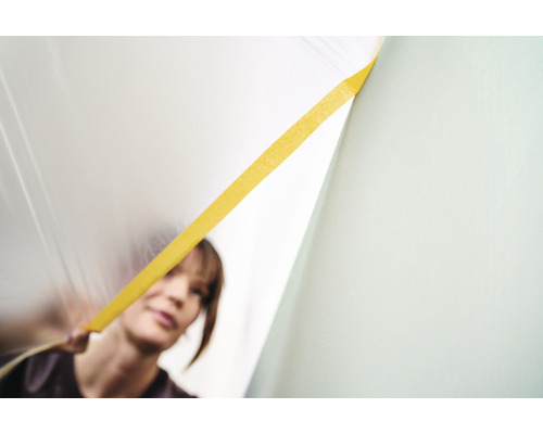 Vrouw bevestigt afdekfolie met plakband aan de muur