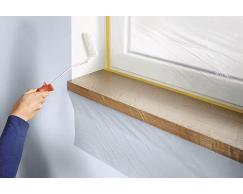 Muur schilderen met verfroller, ramen en vensterbank afgedekt met folie en tape.