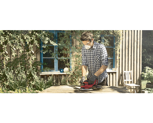 Een man schuurt hout met een elektrische schuurmachine buitenshuis