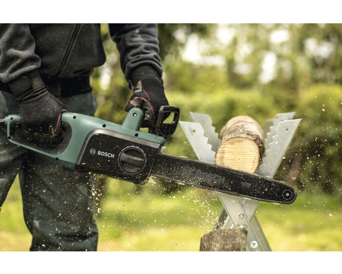 Een persoon zaagt met een elektrische kettingzaag een stuk hout op een zaagbok. Bosch logo.