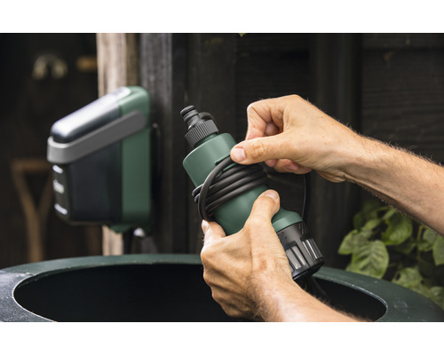 Scène met een man die een regensensor bevestigt aan een regenton en een watergeefcomputer.