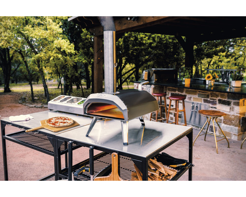 Ooni pizzaoven op een tafel met pizza, ingrediënten en hout