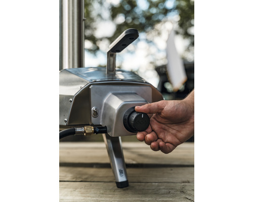 Gedetailleerde opname van een gaspizzaoven met een hand op de bedieningsknop voor temperatuurregeling.