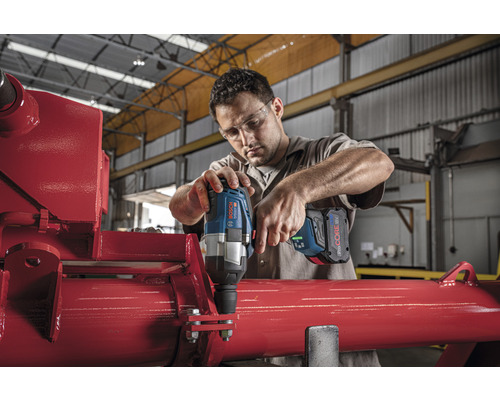 Man werkt met een draadloze slagschroevendraaier aan een rode metalen constructie.
