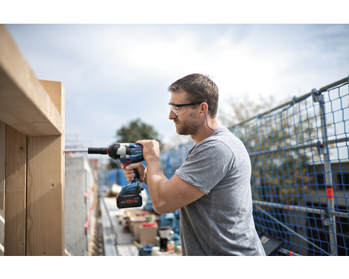 Man met veiligheidsbril, gehoorbescherming en accuslagschroevendraaier aan het werk aan een houten constructie