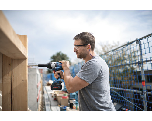Vakman met veiligheidsbril en gehoorbescherming werkt met een accuslagschroevendraaier aan een houten frame