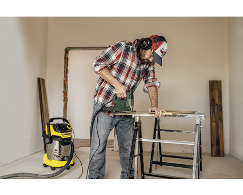 Man werkt met een decoupeerzaag aan een werkstuk op een werkbank, met een stofzuiger op de achtergrond.