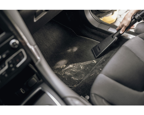 Iemand zuigt de vuile voetruimte van een auto schoon met een stofzuiger.