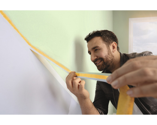 Een man gebruikt schilderstape om een muur voor te bereiden voor het schilderen.