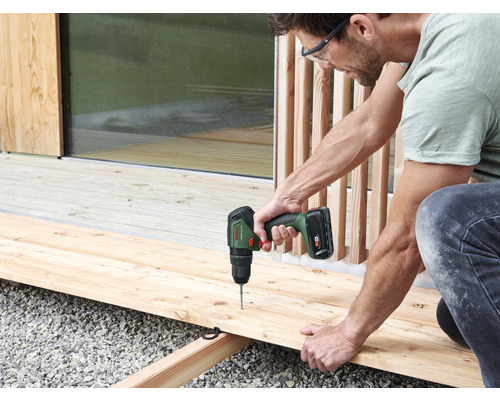 Een man werkt met een accuschroevendraaier aan een houten terras.