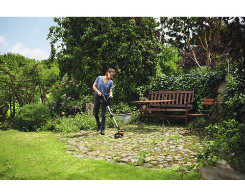 Een vrouw gebruikt een grastrimmer in een groene tuin met bloemen en bomen