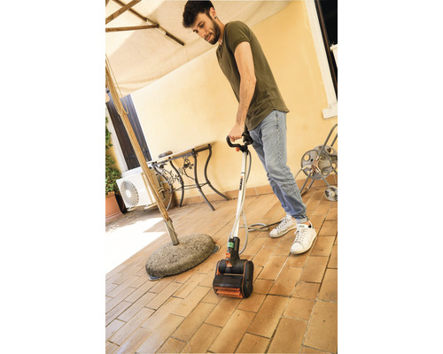 Man gebruikt een elektrische terrasreiniger op een betegeld terras.