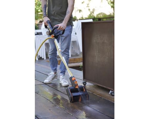 Een persoon reinigt een houten terras met een terrasreiniger van Worx.