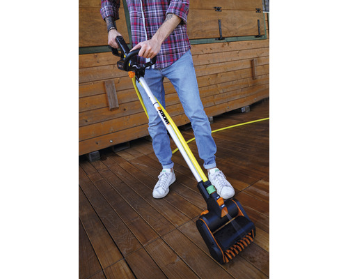 Een persoon reinigt een houten terras met een elektrische borstel. De borstel heeft een lange steel en een borstelkop.