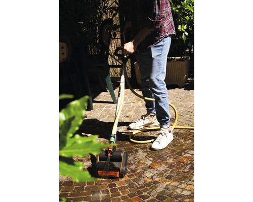 Man reinigt stenen met een terrasreiniger en waterslang in de tuin