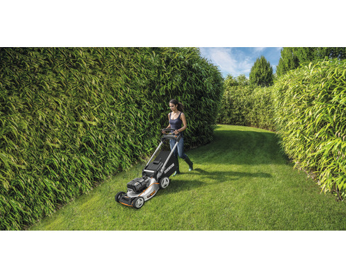 Een vrouw maait het gazon met een grasmaaier in een tuin met bamboehagen.