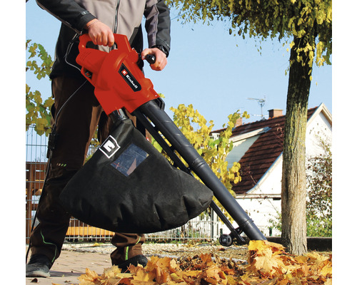 Iemand gebruikt een Einhell bladzuiger om bladeren in de tuin op te zuigen.