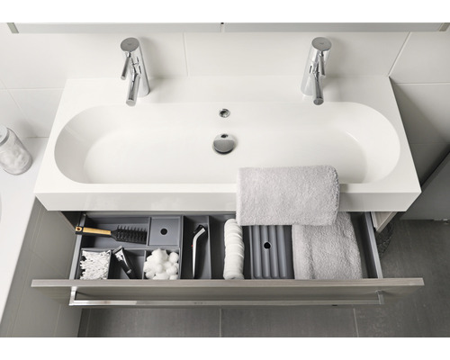 Badkamerwastafel met twee kranen en open lade gevuld met diverse badkamerbenodigdheden