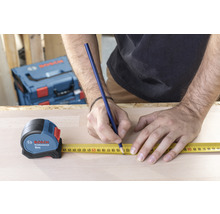 Een persoon meet een houten plank met een Bosch rolmaat en een potlood.