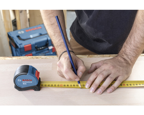 Een persoon meet een houten plank met een Bosch rolmaat en een potlood.