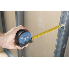 Hand houdt Bosch rolmaat van 5 meter lang vast aan metalen frame