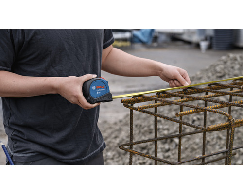 Een persoon meet stalen wapening met een Bosch rolmaat van acht meter lang.