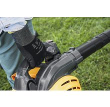 Iemand bedient een bladblazer in de tuin en draagt daarbij handschoenen.