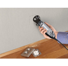 Een persoon snijdt met een Dremel gereedschap een gat in een muur voor een stopcontact.