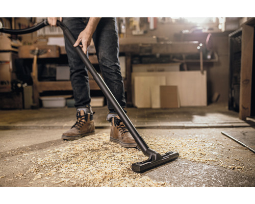 Een persoon zuigt houtsnippers op met een stofzuiger in een werkplaats.