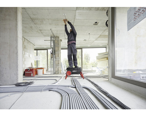 Elektricien op werkzitje installeert elektrische leidingen in een onafgewerkt gebouw