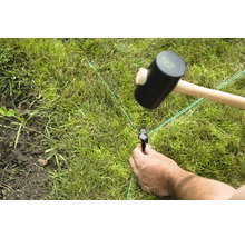 Iemand slaat een haring in het gazon met een rubberen hamer voor tuinplanning