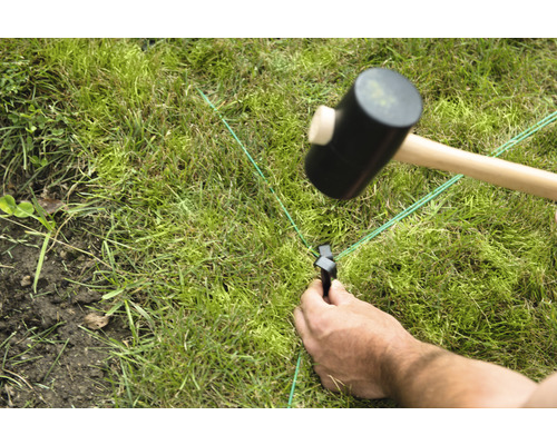 Iemand slaat een haring in het gazon met een rubberen hamer voor tuinplanning
