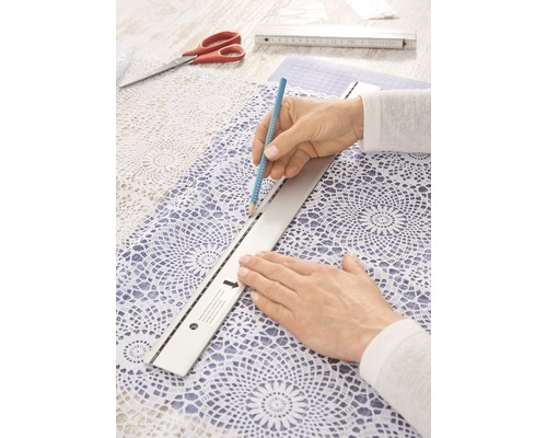 Persoon tekent met potlood en liniaal op tafelkleed van kant