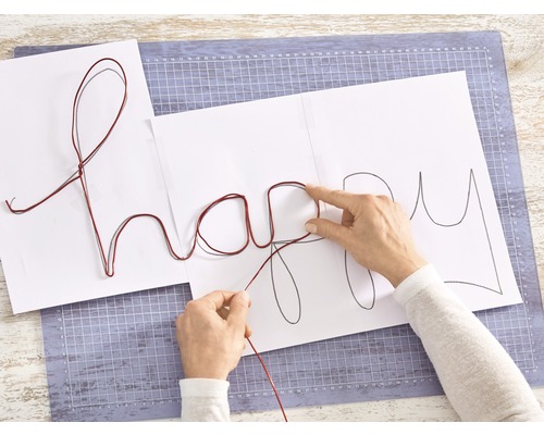 Vrouw vormt met draad het woord Happy op papier