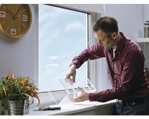 Een man monteert een transparante raambeveiliging in een interieur.