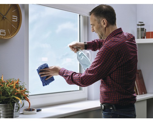 Man maakt raam schoon met spuitfles en doek