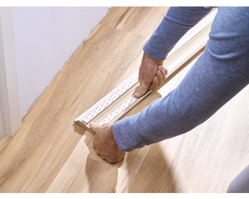 Persoon bevestigt plint met plakstrips aan de vloer.
