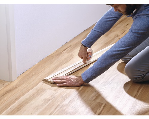 Een persoon bevestigt een plint met tape aan een houten vloer.